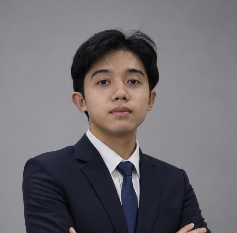 James, in a navy suit and tie, arms crossed, against a plain grey backdrop.